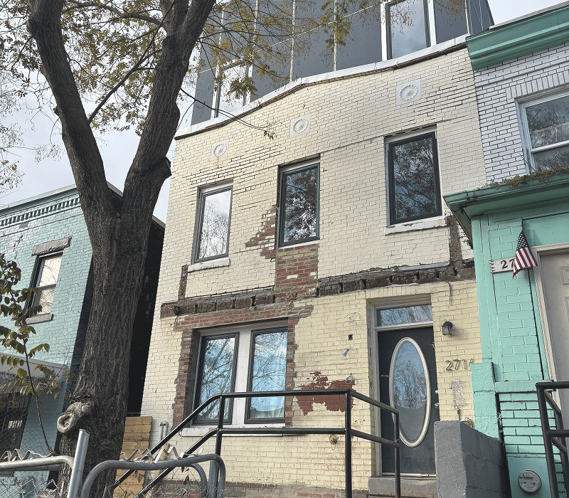 Yellow brick rowhouse with peeling paint and tree
